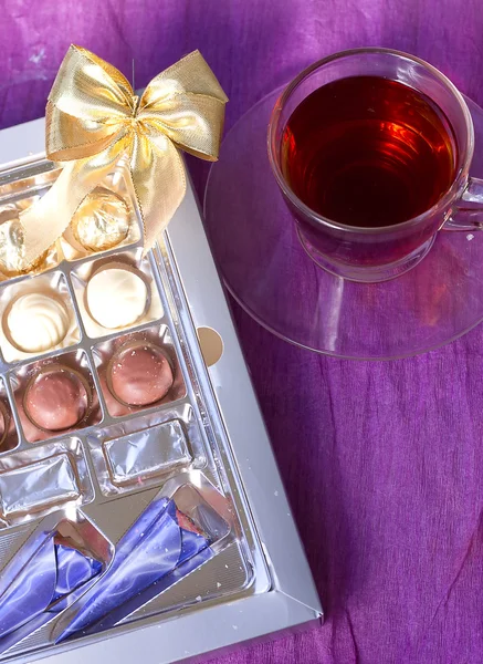 Uma caixa de chocolates com um arco em torno de uma xícara de chá — Fotografia de Stock