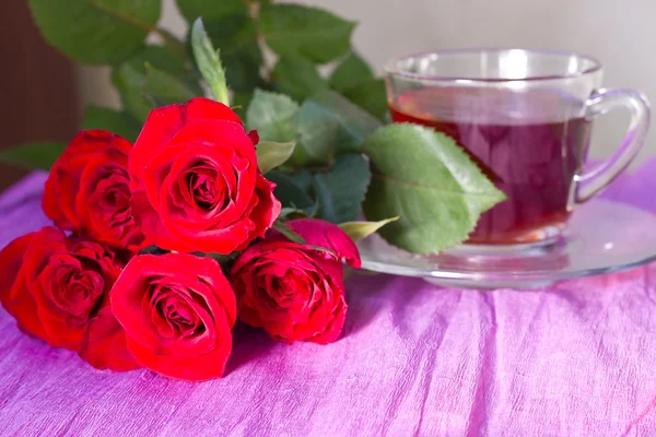 Strauß roter Rosen um Tassen Tee — Stockfoto