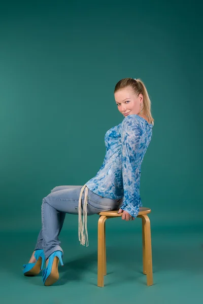 Menina de blusa azul e jeans, sentada em uma cadeira — Fotografia de Stock