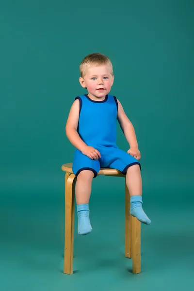 Menino em uma roupa azul sentado em uma cadeira de madeira — Fotografia de Stock