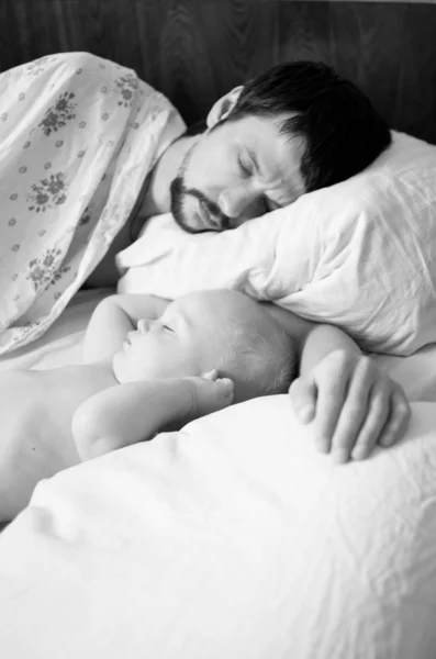 Um pai cansado e bebê filho dormindo, preto e branco, foco no bebê — Fotografia de Stock
