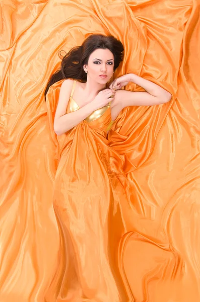Девушка лежит на оранжевом атласе — стоковое фото