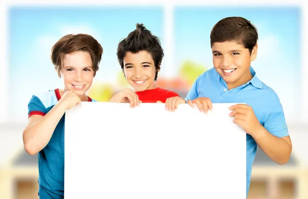Três meninos na sala de aula segurando placa limpa branca — Fotografia de Stock
