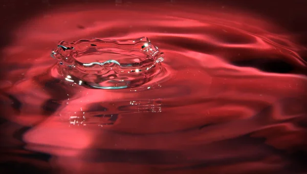 Fröccsenő víz cseppek, piros háttér — Stock Fotó