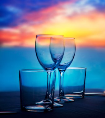 Dish of cups and crystal glasses on sea sunset clipart