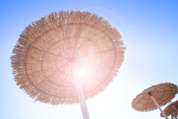 Зонтик на крыше хижины на сухой траве с бликом от объектива — стоковое фото