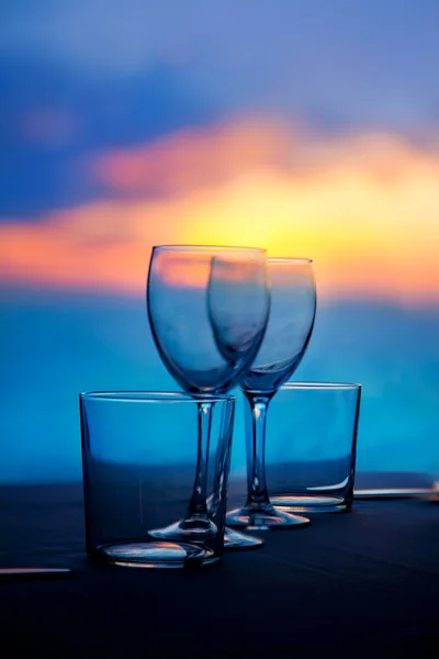 Schotel van kopjes en kristallen glazen op zee zonsondergang — Stockfoto