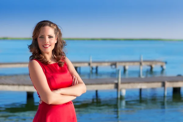 Brunette kvinde kjole i rødt smilende afslappet på en sø - Stock-foto