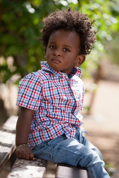 Retrato ao ar livre de um bebê preto situado em um banco — Fotografia de Stock