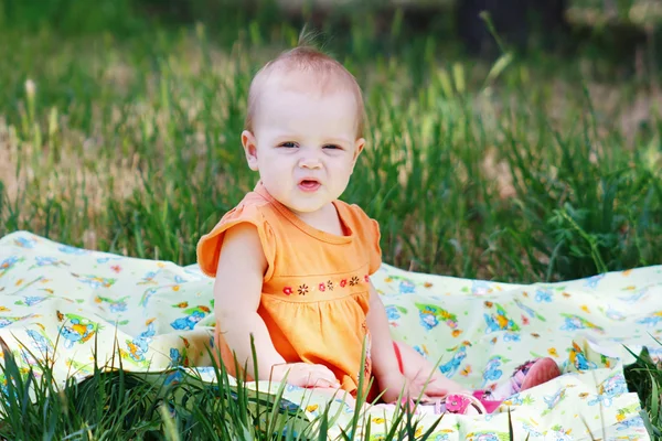 Beautiful little blonde girl in orange dress sitting on a meadow