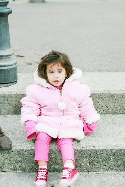 Маленькая девочка в зимней одежде, сидящая на лестнице и глядящая в окно — стоковое фото