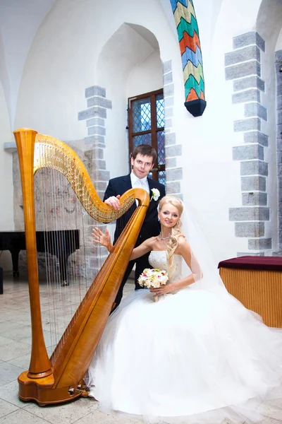 Groom and bride with harp in old town hall interior — Stock Photo, Image