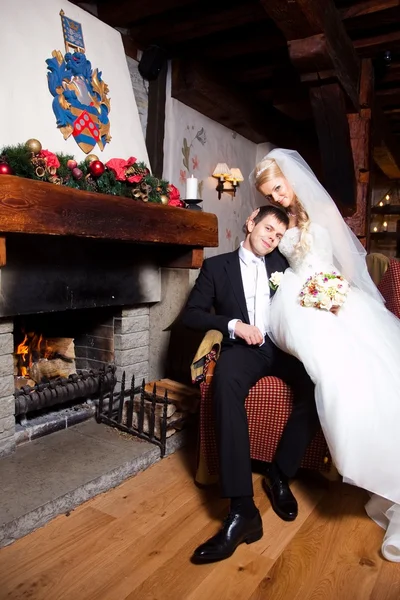 Beautiful groom and bride sitting near fireplace — Stock Photo, Image
