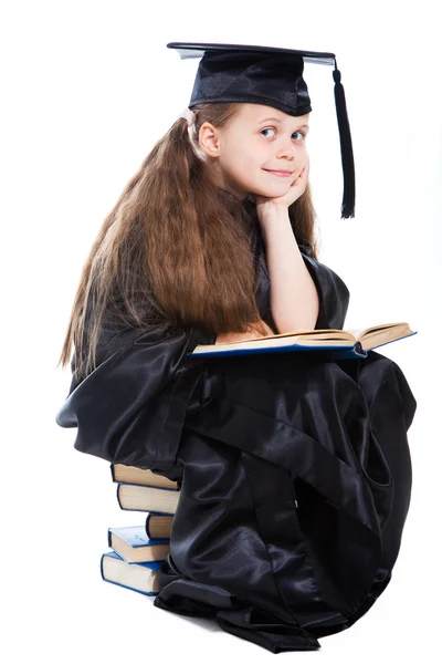 Girl in black academic cap and gown reading big blue book — Stock Photo, Image
