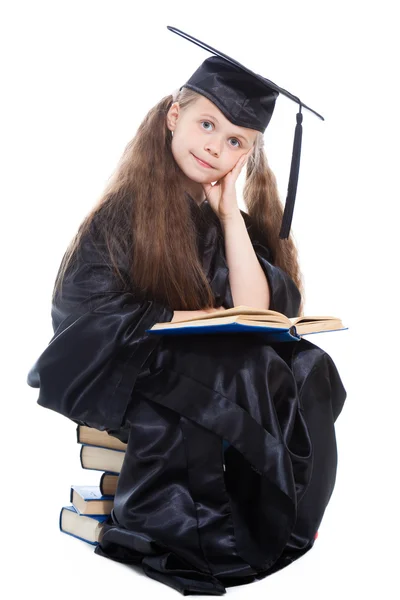 Mädchen in schwarzer akademischer Mütze und Kleid liest großes blaues Buch — Stockfoto