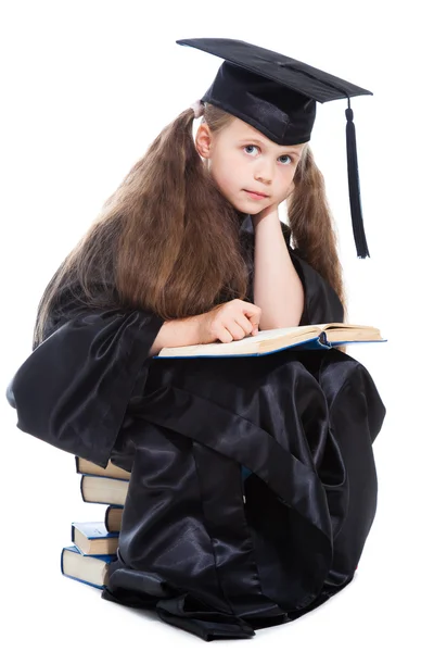 Menina em boné acadêmico preto e vestido de leitura grande livro azul — Fotografia de Stock