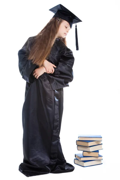 Девушка в черной академической шапочке и платье глядя на кучу книг — стоковое фото