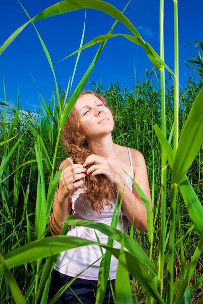 Schöne Mädchen flechten einen Zopf inmitten des hohen grünen Grases der Sommerwiese — Stockfoto