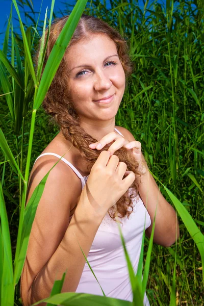 Krásná dívka pletení pletenec mezi vysokou trávou letní louky — Stock fotografie
