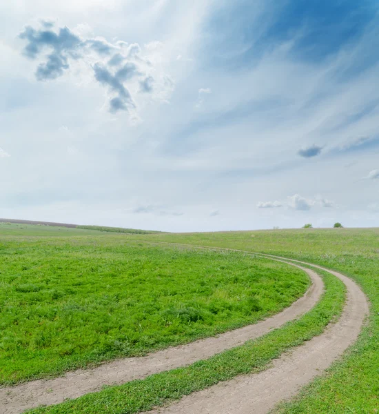 Groen veld met vuile weg onder bewolkte hemel — Stockfoto