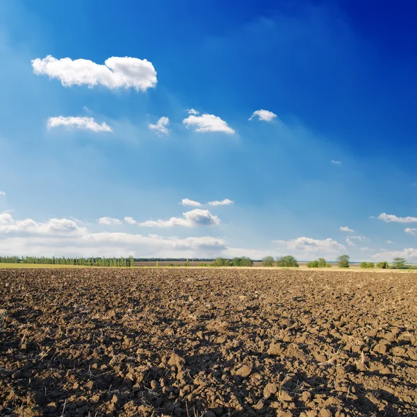 Svart plogad fältet under djupa blå himmel med moln — Stockfoto