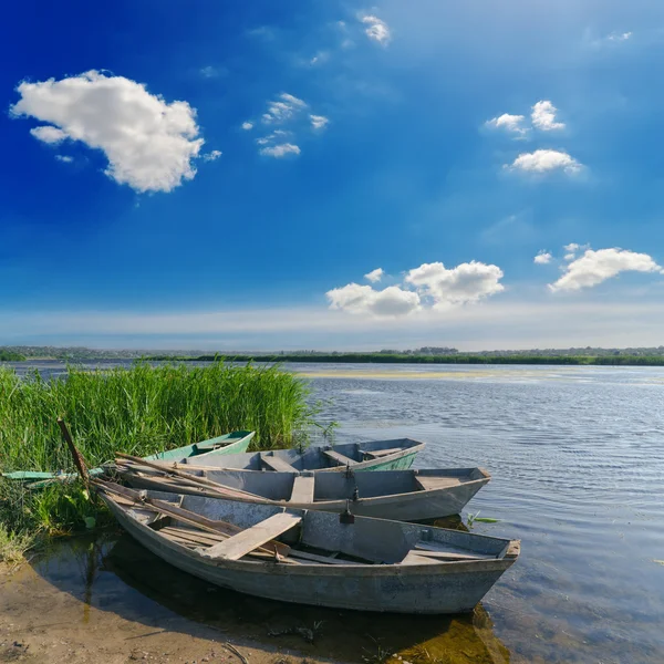 Красива річка і старі човни біля зеленої трави під хмарним небом — стокове фото