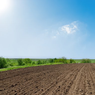 Black ploughed field under deep blue sky with sun clipart