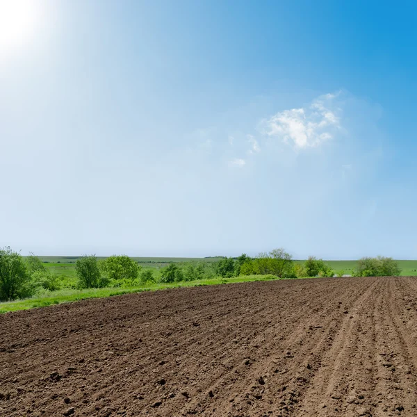 stock image Black ploughed field under deep blue sky with sun