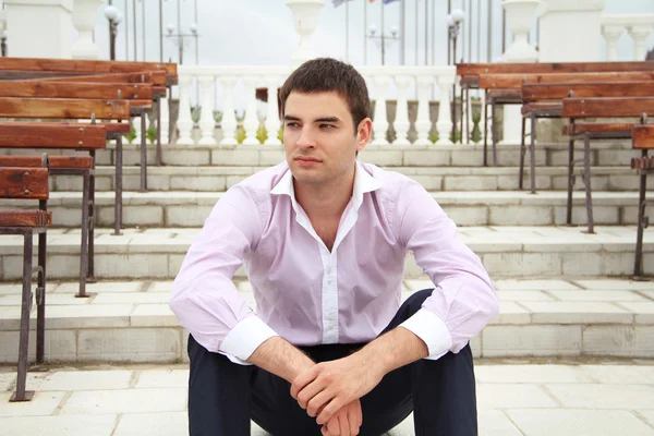 Retrato de jovem homem de negócios sentado em degraus olhando para o lado e pensando — Fotografia de Stock