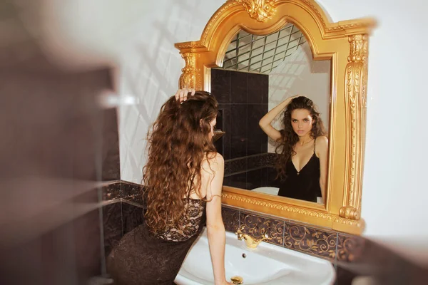 Женщина смотрит на зеркало с роскошной рамкой — стоковое фото