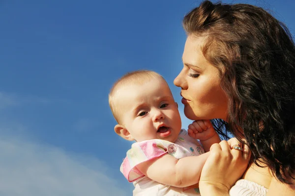 Szczęśliwa matka całuje dziecko nad niebieski niebo — Zdjęcie stockowe