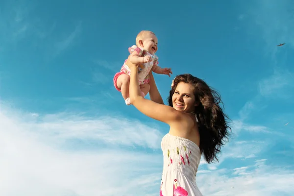 Mãe feliz brincando com o bebê sobre o céu azul — Fotografia de Stock