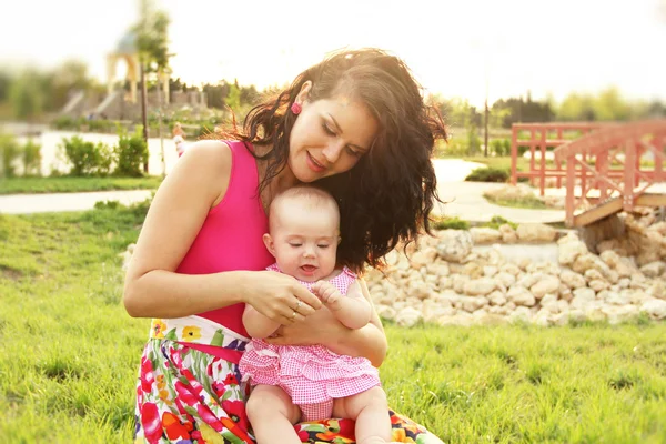 Vacker ung mamma med dotter avkopplande sittande gräs — Stockfoto
