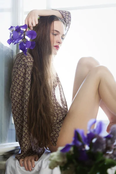 Flicka med blommor i fönstret — Stockfoto