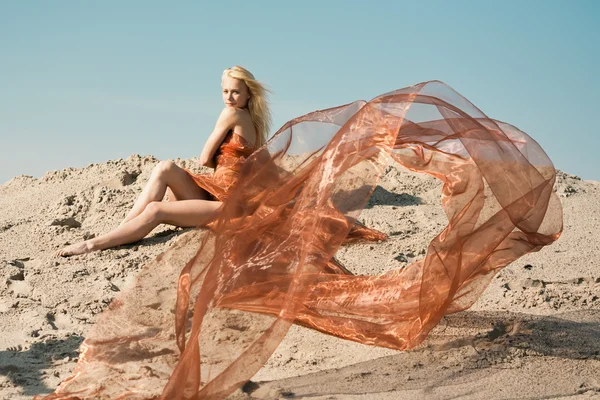 Девушка лежит на песке в оранжевой ткани — стоковое фото
