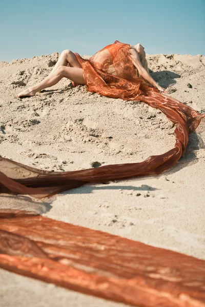 Девушка лежит на песке в оранжевой ткани — стоковое фото