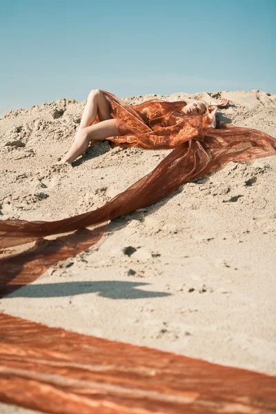 Mädchen liegt in orangefarbenem Tuch auf Sand — Stockfoto