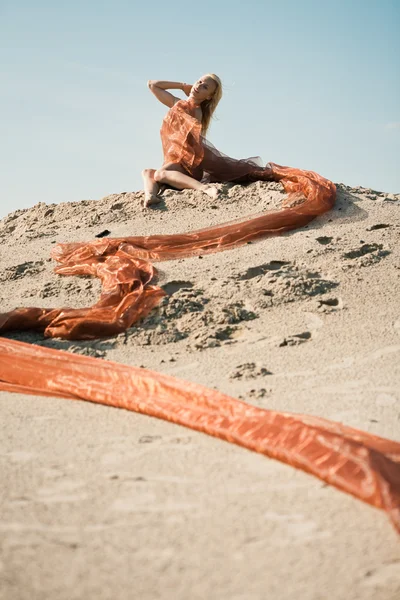Дівчина лежить на піску в помаранчевій тканині — стокове фото