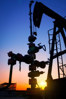 An oil pump jack is silhouetted by the setting sun clipart