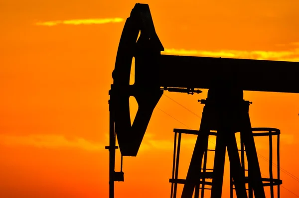 Ein Ölpumpenheber wird von der untergehenden Sonne in Szene gesetzt — Stockfoto