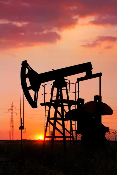 An oil pump jack is silhouetted by the setting sun — Stock Photo, Image