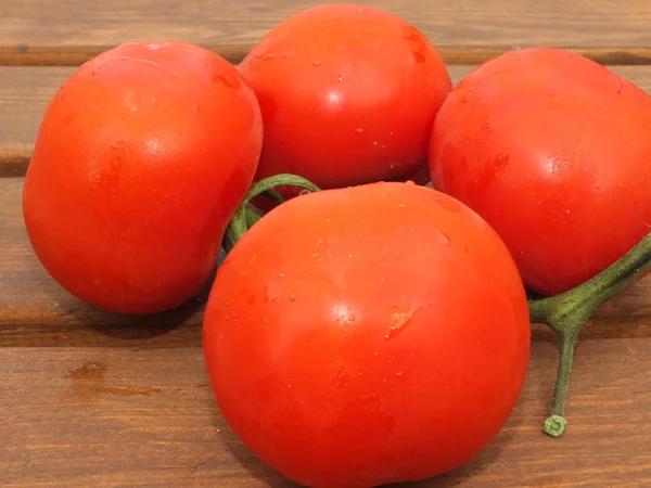 Quatro tomates vermelhos em uma tábua de madeira — Fotografia de Stock