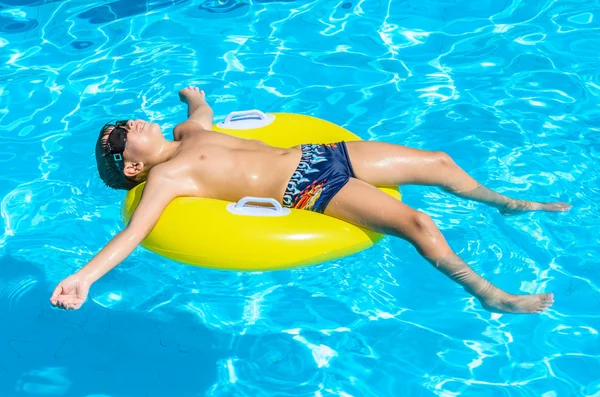 Pojke som flyter på en uppblåsbar cirkel i poolen. Stockbild