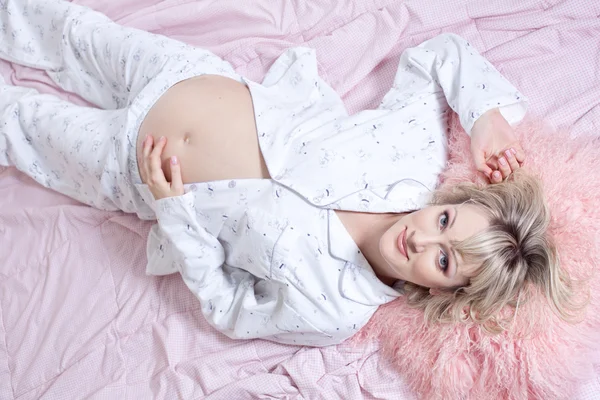 Vakker, gravid kvinne i sengen holder magen – stockfoto