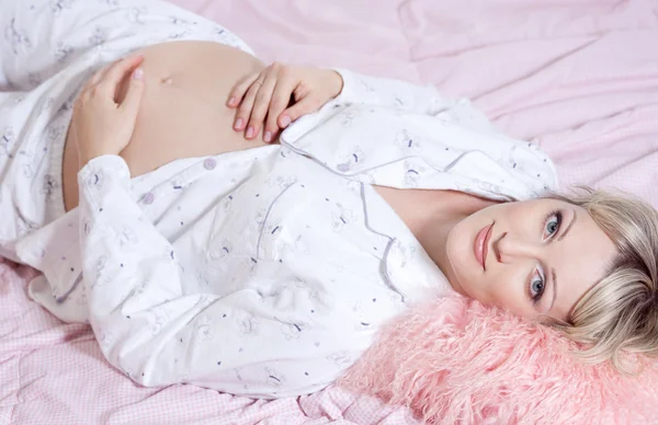 Krásná těhotná žena v posteli drží její břicho — Stock fotografie