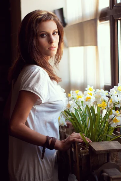Beautiful young woman standing by a window — Stock Photo, Image