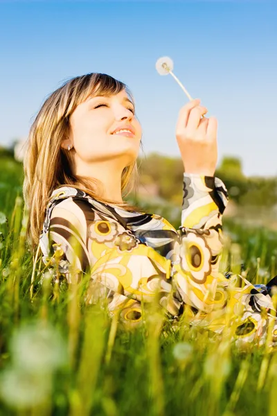 Atractiva chica joven relajándose en un prado, sosteniendo flor de diente de león — Foto de Stock