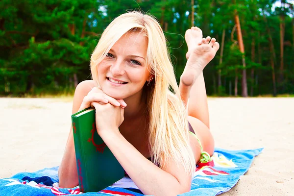 En kvinna i en baddräkt på en strand som läser en bok — Stockfoto