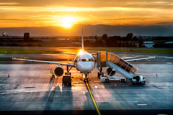 Літак біля терміналу в аеропорту на заході сонця — стокове фото