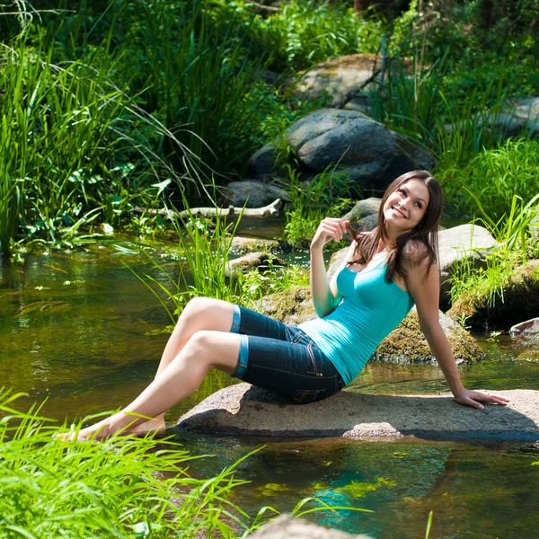 川のそばに座っている若い幸せな美しい女性は — ストック写真